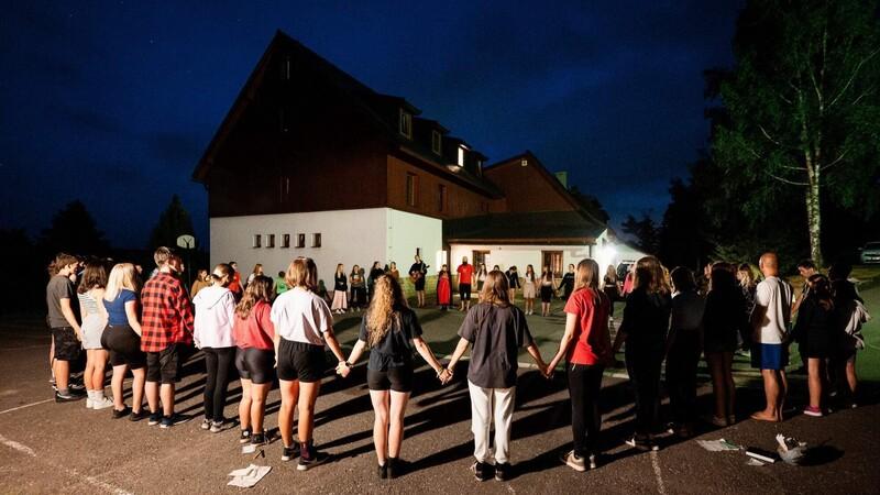 Skupina mladých modlícíc se ve tmě a držící se za ruce.